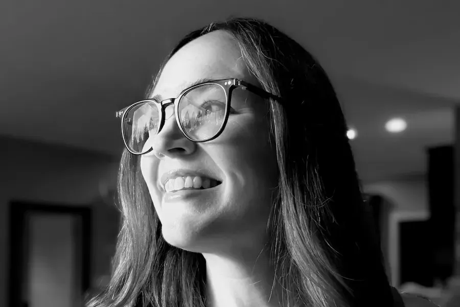 black and white headshot of a smiling woman with long hair wearing glasses looking off camera